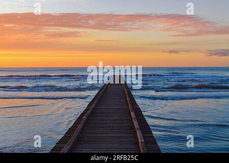 Un meraviglioso e scintillante cielo all'alba sulla spiaggia e il molo di legno del Lido di Jesolo, popolare località estiva sulla costa adriatica, vicino a Venezia, Veneto, Italia. Foto Stock