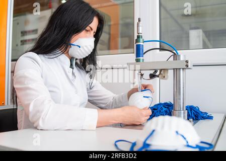 La ragazza lavora alla macchina per la fabbricazione di maschere mediche con nanofibra e saldare i loop a loro con ultrasuoni. Coronovirus e Covid- Foto Stock