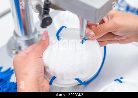 La ragazza lavora alla macchina per la fabbricazione di maschere mediche con nanofibra e saldare i loop a loro con ultrasuoni. Coronovirus e Covid- Foto Stock