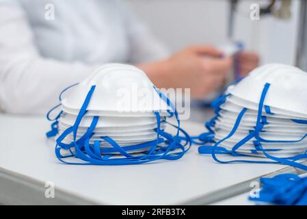 La ragazza lavora alla macchina per la fabbricazione di maschere mediche con nanofibra e saldare i loop a loro con ultrasuoni. Coronovirus e Covid- Foto Stock