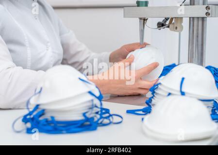 La ragazza lavora alla macchina per la fabbricazione di maschere mediche con nanofibra e saldare i loop a loro con ultrasuoni. Coronovirus e Covid- Foto Stock