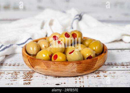 Olive verdi ripiene di pepe in un recipiente di legno. Olive su fondo di legno bianco. Cucina mediterranea. cibo vegano Foto Stock