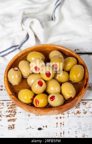 Olive verdi ripiene di pepe in un recipiente di legno. Olive su fondo di legno bianco. Cucina mediterranea. cibo vegano Foto Stock