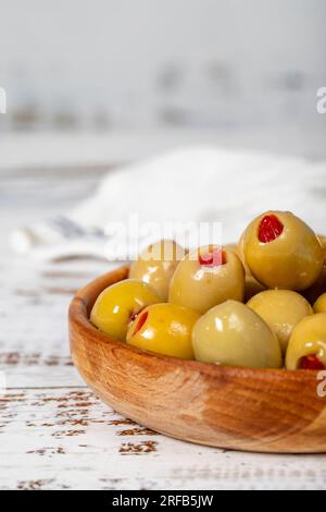 Olive verdi ripiene di pepe in un recipiente di legno. Olive su fondo di legno bianco. Cucina mediterranea. cibo vegano. Primo piano Foto Stock