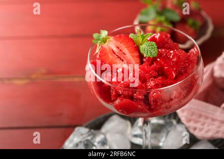 Granita di fragole o sorbetto di frutti di bosco fresco in vetro su vecchio sfondo rosso del tavolo. Consistenza di gelato o sorbetto. Gelato con fragole e mi Foto Stock