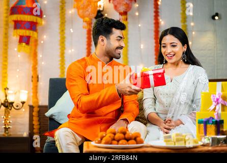 Felice fratello indiano che regala o presenta alla sorella dopo aver legato rakhi a casa durante la festa di raksha bandhan - confuso dell'amore dei fratelli Foto Stock