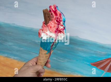 Mano che tiene il gelato alla fragola contro la spiaggia di Seaside Foto Stock