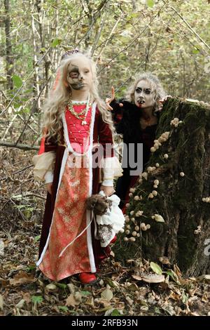 Una donna sotto forma di vampiro o strega sta per mordere una principessa con un trucco fiabesco e un abito medievale. La strega sta guardando il gi Foto Stock