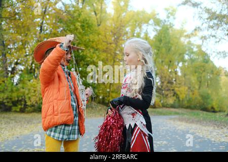 Bambina con una giacca arancione e un cappello da cowboy mostra alla sua amica in costume da cheerleader i suoi scheletri su una corda. Festa di Halloween. P orizzontale Foto Stock