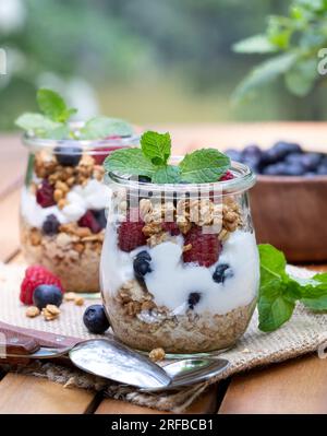 Parfait di yogurt con muesli, mirtilli e lamponi guarniti con menta all'aperto su un tavolo da patio in legno Foto Stock