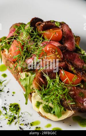 Bruschetta con succosa carne, pomodori, erbe, formaggio, salsa al pesto su un piatto bianco. Primo piano. Foto Stock