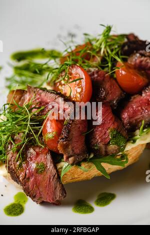 Bruschetta con succosa carne, pomodori, erbe, formaggio, salsa al pesto su un piatto bianco. Primo piano. Foto Stock
