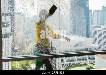 Pulitore thailandese delle finestre che lavora su un alto edificio affacciato sull'area di Sukhumvit, Bangkok, Thailandia Foto Stock