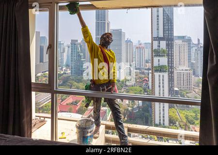 Pulitore thailandese delle finestre che lavora su un alto edificio affacciato sull'area di Sukhumvit, Bangkok, Thailandia Foto Stock