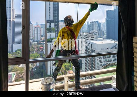 Pulitore thailandese delle finestre che lavora su un alto edificio affacciato sull'area di Sukhumvit, Bangkok, Thailandia Foto Stock