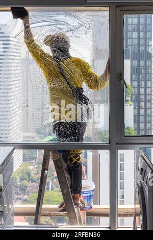 Pulitore thailandese delle finestre che lavora su un alto edificio affacciato sull'area di Sukhumvit, Bangkok, Thailandia Foto Stock