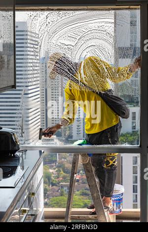 Pulitore thailandese delle finestre che lavora su un alto edificio affacciato sull'area di Sukhumvit, Bangkok, Thailandia Foto Stock