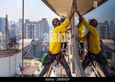 Pulitore thailandese delle finestre che lavora su un alto edificio affacciato sull'area di Sukhumvit, Bangkok, Thailandia Foto Stock