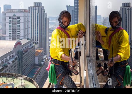 Pulitore thailandese delle finestre che lavora su un alto edificio affacciato sull'area di Sukhumvit, Bangkok, Thailandia Foto Stock