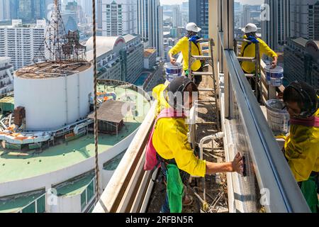 Pulitore thailandese delle finestre che lavora su un alto edificio affacciato sull'area di Sukhumvit, Bangkok, Thailandia Foto Stock