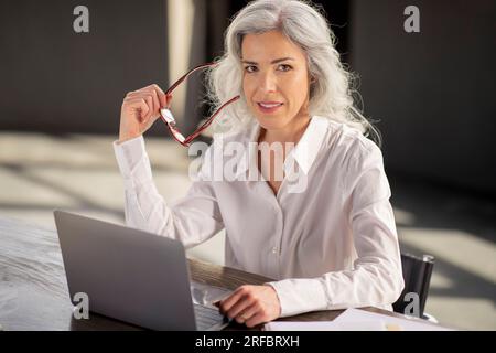 Donna d'affari in posa con occhiali da vista seduti con un notebook in un ufficio moderno Foto Stock