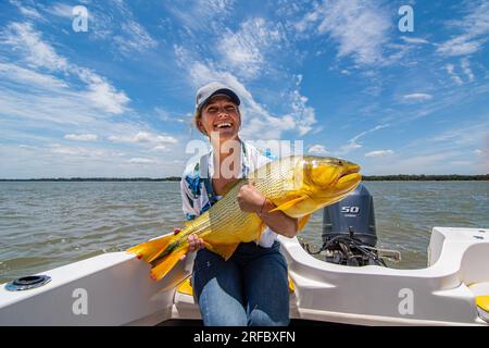 Giovane donna bianca che detiene un grande esemplare di dorado dorato (Salminus Brasiliensis) durante una giornata di pesca. Foto Stock