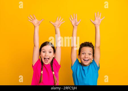 Foto di graziosi bambini preadolescenti eccitati che indossano t-shirt che urlano braccia in aumento, sfondo giallo isolato Foto Stock