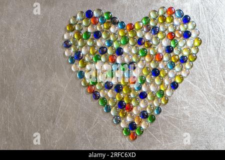 Cuore fatto di pietre artificiali colorate su sfondo argento. San Valentino. Festa della mamma. Tema d'amore. Foto Stock