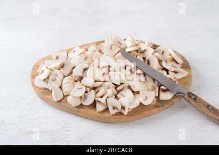 Tavola di legno con funghi champignon a fette su sfondo grigio chiaro, cucina cibo vegano. Foto Stock