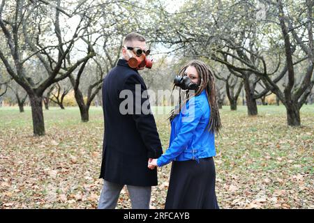 Una donna con dreadlock e una maschera antigas tiene la mano di un uomo con occhiali steampunk e una maschera antigas. L'amore in un disastro ecologico. Foto orizzontale Foto Stock