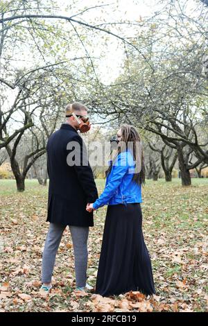 Una donna con dreadlock e una maschera antigas tiene la mano di un uomo con occhiali steampunk e una maschera antigas. L'amore in un disastro ecologico. Foto verticale Foto Stock