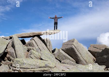 Bilanciare la roccia sulla cima di Glyder Fach con una persona in piedi sulla cima. Foto Stock