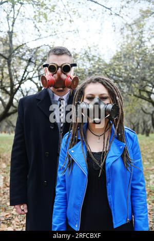 Una donna con dreadlock e una maschera a gas e un uomo con occhiali a forma di steampunk e una maschera a gas guarda la macchina fotografica e posa nel parco autunnale. disa ecologica Foto Stock