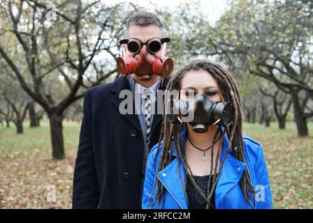 Una donna con dreadlock e una maschera a gas e un uomo con occhiali a forma di steampunk e una maschera a gas guarda la macchina fotografica e posa nel parco autunnale. disa ecologica Foto Stock