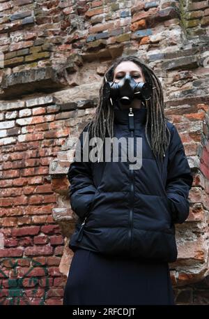 Ritratto drammatico di una donna che indossa una maschera a gas in un edificio in rovina. Foto verticale Foto Stock