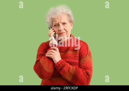 Donna anziana triste che parla dal telefono cellulare su sfondo verde Foto Stock