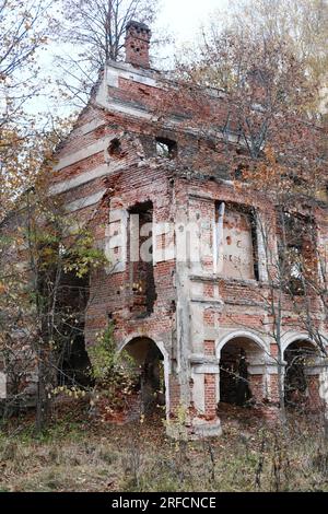 Vecchio edificio in mattoni in rovina con archi nella foresta autunnale. Esterno dell'edificio. Foto verticale Foto Stock