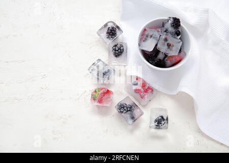 Ciotola con frutti di bosco congelati in cubetti di ghiaccio su sfondo bianco Foto Stock