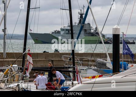 I diportisti preparano le barche per le regate della settimana di cowes sull'isola di wight con la HMS Tyne, la nave da pattuglia della marina reale sullo sfondo. Foto Stock