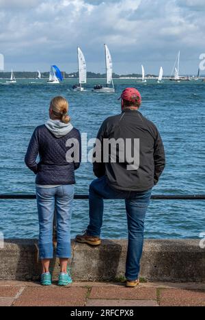 coppia di mezza età in piedi sul lungomare a cowes sull'isola di wight guardando gli yacht che gareggiano durante la regata annuale della settimana di cowes. Foto Stock