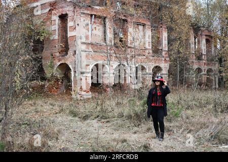 Una donna a immagine del barone Saturday si pone sullo sfondo di un vecchio edificio in mattoni in rovina. La modella indossa un corsetto, un cardigan e un top h. Foto Stock