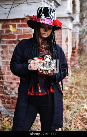 Una donna a immagine del barone Saturday. Il modello è vestito con un corsetto, un cardigan e un cappello decorato con figure scheletriche e pose con un ci Foto Stock