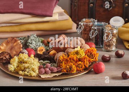 Materiale vegetale per la tintura organica di tessuti su un piatto sul mucchio di fondo di tessuti tinti a mano e vasi di erba secca Foto Stock