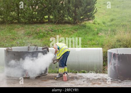 Installazione di un tubo di cemento nel terreno per raccogliere l'acqua piovana. Il lavoratore taglia i fori nella parte in cemento del tubo per collegarlo al drenaggio. A Foto Stock