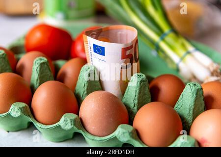 Un concetto di costo della vita, inflazione alimentare con banconote in euro in un pacchetto di uova e altri generi alimentari. Foto Stock