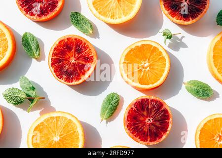 Vari tipi di agrumi a fette, arance rosse con foglie di menta verde su sfondo bianco con ombre dure. Vista dall'alto, base piatta. Foto Stock