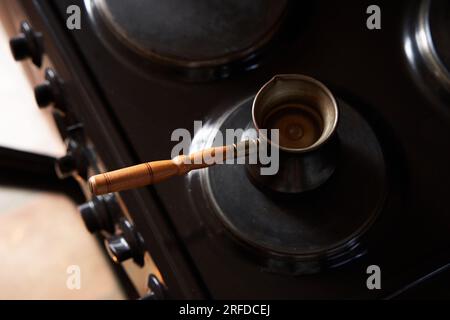 Un uomo che prepara un caffè nero sulla stufa elettrica. Prepara il caffè in una caffettiera turca. Foto Stock