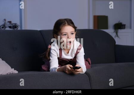 Una ragazza scioccata che guarda la TV sul divano a casa Foto Stock