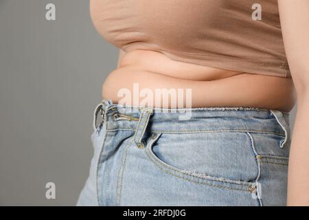 Donna in sovrappeso con jeans stretti su sfondo grigio, primo piano. Spazio per il testo Foto Stock