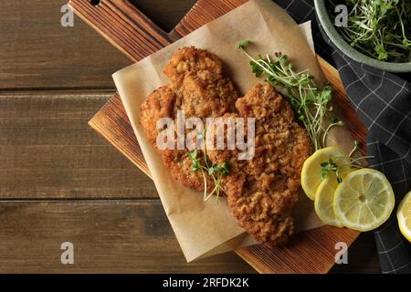 Gustosi schnitzels serviti con limone e microgreen su un tavolo di legno, piatti. Spazio per il testo Foto Stock